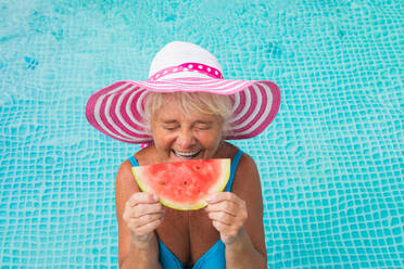 Happy senior woman having party in the swimming pool - Beautiful senior lady sunbathing and relaxing in a private pool during summertime - DMDF02708