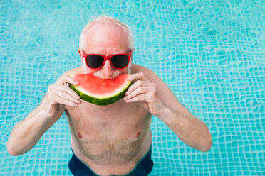 Happy senior man having party in the swimming pool - Active elderly male person sunbathing and relaxing in a private pool during summertime - DMDF02710
