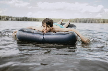 Happy teenager lying on inflatable raft in sea - ANAF01947
