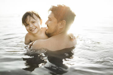 Glücklicher Vater mit Sohn beim Schwimmen im Wasser an einem sonnigen Tag - ANAF01952