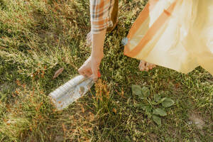 Hand eines Jungen, der eine Plastikflasche im Gras aufhebt - ANAF01956