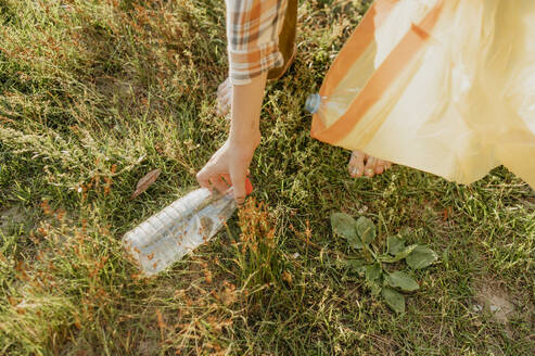 Hand of boy picking up plastic bottle on grass - ANAF01956