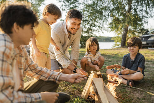 Happy father and children roasting sausages in bonfire - ANAF01963