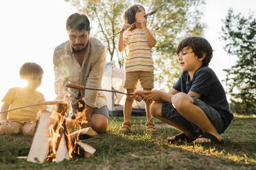 Vater und Kinder rösten beim Picknick Würstchen am Lagerfeuer - ANAF01964