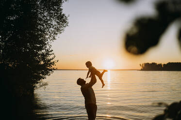 Vater hält Sohn vor dem Meer bei Sonnenuntergang - ANAF01970