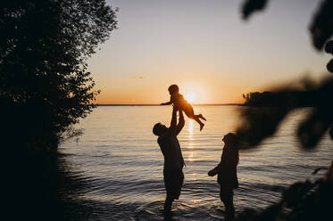 Mutter mit Vater hält Sohn vor dem Meer bei Sonnenuntergang - ANAF01971