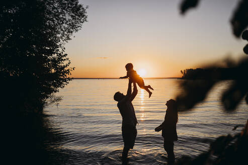 Mother with father holding son in front of sea at sunset - ANAF01971