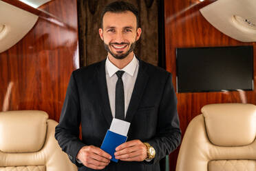 Gut aussehender Geschäftsmann in elegantem Anzug, der in einem exklusiven Privatjet fliegt - Erfolgreicher Unternehmer sitzt in der exklusiven Business Class im Flugzeug, Konzepte für Geschäft und Transport - DMDF02772