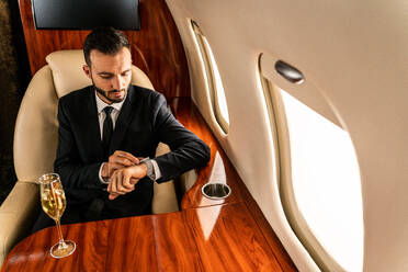 Gut aussehender Geschäftsmann in elegantem Anzug, der in einem exklusiven Privatjet fliegt - Erfolgreicher Unternehmer sitzt in der exklusiven Business Class im Flugzeug, Konzepte für Geschäft und Transport - DMDF02776