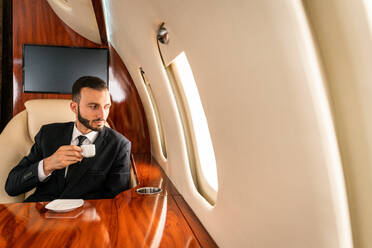 Gut aussehender Geschäftsmann in elegantem Anzug, der in einem exklusiven Privatjet fliegt - Erfolgreicher Unternehmer sitzt in der exklusiven Business Class im Flugzeug, Konzepte für Geschäft und Transport - DMDF02785