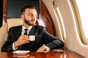 Gut aussehender Geschäftsmann in elegantem Anzug, der in einem exklusiven Privatjet fliegt - Erfolgreicher Unternehmer sitzt in der exklusiven Business Class im Flugzeug, Konzepte für Geschäft und Transport - DMDF02786