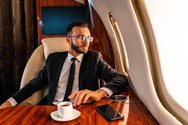 Gut aussehender Geschäftsmann in elegantem Anzug, der in einem exklusiven Privatjet fliegt - Erfolgreicher Unternehmer sitzt in der exklusiven Business Class im Flugzeug, Konzepte für Geschäft und Transport - DMDF02792