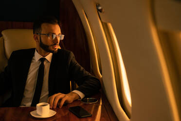 Gut aussehender Geschäftsmann in elegantem Anzug, der in einem exklusiven Privatjet fliegt - Erfolgreicher Unternehmer sitzt in der exklusiven Business Class im Flugzeug, Konzepte für Geschäft und Transport - DMDF02793