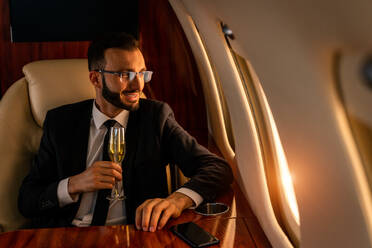 Gut aussehender Geschäftsmann in elegantem Anzug, der in einem exklusiven Privatjet fliegt - Erfolgreicher Unternehmer sitzt in der exklusiven Business Class im Flugzeug, Konzepte für Geschäft und Transport - DMDF02795