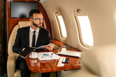Gut aussehender Geschäftsmann in elegantem Anzug, der in einem exklusiven Privatjet fliegt - Erfolgreicher Unternehmer sitzt in der exklusiven Business Class im Flugzeug, Konzepte für Geschäft und Transport - DMDF02798