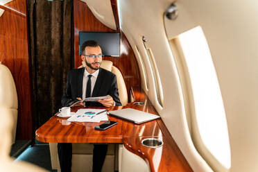 Gut aussehender Geschäftsmann in elegantem Anzug, der in einem exklusiven Privatjet fliegt - Erfolgreicher Unternehmer sitzt in der exklusiven Business Class im Flugzeug, Konzepte für Geschäft und Transport - DMDF02799