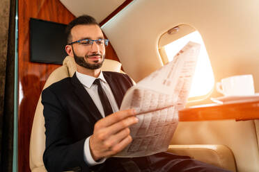 Gut aussehender Geschäftsmann in elegantem Anzug, der in einem exklusiven Privatjet fliegt - Erfolgreicher Unternehmer sitzt in der exklusiven Business Class im Flugzeug, Konzepte für Geschäft und Transport - DMDF02800