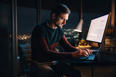Professioneller kaukasischer Geschäftsmann, der bis spät in die Nacht in einem Büro arbeitet und an seinem Laptop für ein digitales Marketingprojekt tippt. Kreativer Unternehmer, der stundenlang arbeitet, um eine Frist einzuhalten. - JLPSF30734
