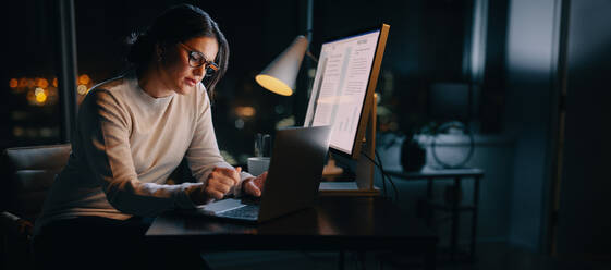 Kaukasische Frau arbeitet bis spät in die Nacht von ihrem Heimbüro aus und tippt ihre Ideen auf ihrem Laptop ein. Professionelle Geschäftsfrau, die bis spät in die Nacht arbeitet, ihre Work-Life-Balance aufrechterhält und sich im digitalen Marketing auszeichnet. - JLPSF30740