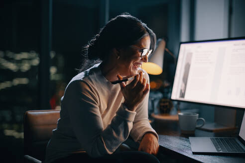 Professional woman working late in her home office, making phone calls to discuss a project with her colleagues. Happy business woman showing commitment and dedication to her work. - JLPSF30744