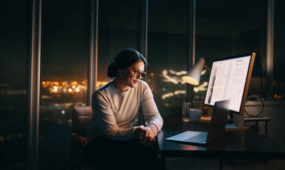 Eine Geschäftsfrau, die zu später Stunde ein virtuelles Meeting auf ihrem Laptop abhält. Eine Mitarbeiterin, die in ihrem Heimbüro sitzt und per Online-Videokonferenz Geschäftsprojekte bespricht. - JLPSF30750