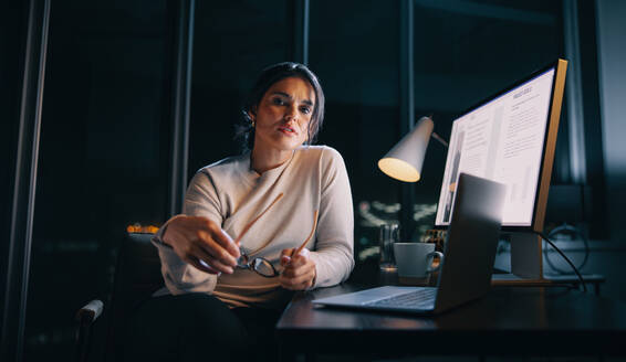 Determined businesswoman balances work and home life, putting in late hours at her home office. Woman working with her laptop and computer, planning and managing projects as a marketing manager. - JLPSF30758