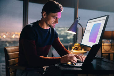 Ein kaukasischer Geschäftsmann sitzt nachts an seinem Schreibtisch in einem Büro und benutzt einen Laptop für Marktanalysen und -forschung. Ein professioneller Mann arbeitet bis spät in die Nacht und tippt mit Entschlossenheit, um die Frist einzuhalten. - JLPSF30772