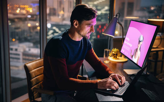 VR developer and designer working late in his office, using a laptop and a computer at his desk. He is dedicated, creative, and focused on completing projects and meeting deadlines. - JLPSF30773