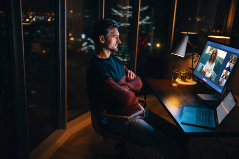 Ein Geschäftsmann, der an seinem Schreibtisch im Büro sitzt, der nachts an einer Online-Sitzung mit seinen Kollegen teilnimmt, ein Berufstätiger, der viele Stunden arbeitet, um mit seinem Team zusammenzuarbeiten und ein Projekt abzuschließen. - JLPSF30778