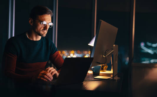Geschäftsmann, der noch spät in seinem Heimbüro arbeitet und eine virtuelle Besprechung mit seinem Team abhält. Berufstätiger Mann, der einen Laptop benutzt, um zu kommunizieren und ein Projekt vor dem Abgabetermin zu planen. - JLPSF30780