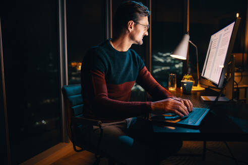 Ein Unternehmer arbeitet spät in der Nacht in einem belebten Büro und tippt auf seinem Laptop, während er plant und Strategien entwickelt. Der schwach beleuchtete Arbeitsbereich ist mit engagierten Fachleuten gefüllt, die sich auf ihre Projekte konzentrieren. Diese Szene fängt die Entschlossenheit und Energie des Arbeitsplatzes ein. - JLPSF30781