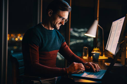 A business man working late from home, typing on a laptop. Dedicated and driven, he prioritizes his project and embraces remote work. - JLPSF30782