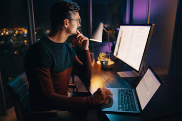 Ein weißer Geschäftsmann arbeitet bis spät in die Nacht im Büro und plant ein Marketingprojekt auf seinem Laptop. Die Atmosphäre ist ruhig und nachdenklich, während er sich auf seine Arbeit konzentriert. - JLPSF30785