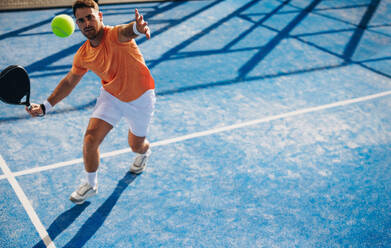 Ein Sportler zeigt sein Können und seine Präzision, als er in einem spannenden Padel-Tennisspiel einen Schuss abgibt. Ein Padel-Tennisspieler dominiert den Platz, während er seinen Schläger in Position hält, bereit, den Ball zu schlagen. Bei diesem Foto wurde absichtlich das Korn des 35-mm-Films verwendet. - JLPPF02347