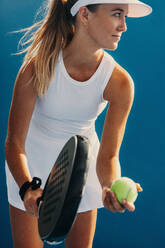 Junge Sportlerin bei einem Padelspiel, die ihren Schläger in Position für einen Vorhandaufschlag hält. Erfahrene Sportlerin bei einem Meisterschaftsspiel. Dieses Foto weist absichtlich eine 35-mm-Filmkörnung auf. - JLPPF02366