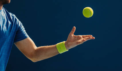 Ein männlicher Tennisspieler fängt einen Tennisball mit einer Hand. Ein Sportler übt seine Fähigkeiten und Techniken, während er auf dem Tennisplatz trainiert. Bei diesem Foto wurde absichtlich das Korn eines 35-mm-Films verwendet. - JLPPF02373