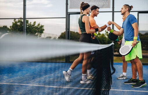Ein Team von Padel-Sportlern, sowohl männlich als auch weiblich, feiert nach einem Doppel-Tennismatch auf einem Padel-Platz. Fäuste ballen und lächeln in dieser Szene der Freundschaft, des Teamworks und des Sportsgeistes. Dieses Foto hat absichtlich 35mm Filmkorn verwendet. - JLPPF02379