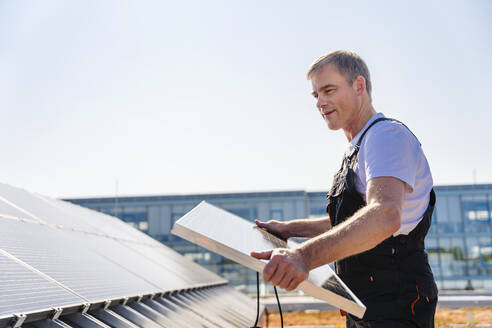 Ein Facharbeiter bei der Montage von Solarmodulen auf dem Dach eines Firmengebäudes - DIGF20251