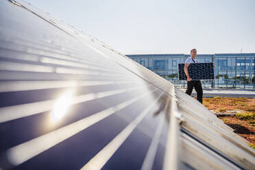 Ein Facharbeiter, der ein Solarmodul zur Installation auf dem Dach eines Gewerbebetriebs transportiert - DIGF20257