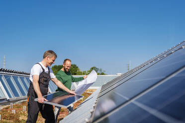 Handwerker und Kollege bei der Installation eines Solarmoduls auf dem Dach des Firmengebäudes als Beitrag zu nachhaltigen Energiepraktiken - DIGF20264