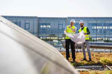 Zwei Techniker analysieren Pläne auf dem Dach eines mit Sonnenkollektoren ausgestatteten Firmengebäudes - DIGF20268