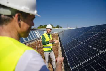 Zwei Techniker besprechen die Installation von Solarmodulen auf dem Dach eines Firmengebäudes - DIGF20274