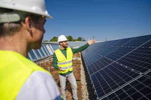 Zwei Techniker diskutieren über die Installation von Solarmodulen auf dem Dach eines Firmengebäudes - DIGF20275