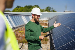 Ein Mann bespricht auf einem mit Sonnenkollektoren geschmückten Dach geschäftliche Angelegenheiten und nutzt einen Tablet-PC, um mit einem Kollegen zu kommunizieren - DIGF20281