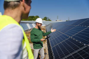Ein Mann bespricht auf einem mit Sonnenkollektoren geschmückten Dach geschäftliche Angelegenheiten und nutzt einen Tablet-PC, um mit einem Kollegen zu kommunizieren - DIGF20282
