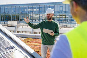 Businessman discussing work on rooftop with solar panels using tablet PC - DIGF20286