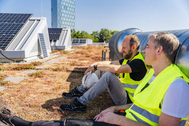 Zwei Solarmodultechniker genießen eine Pause auf dem Dach eines Firmengebäudes - DIGF20289