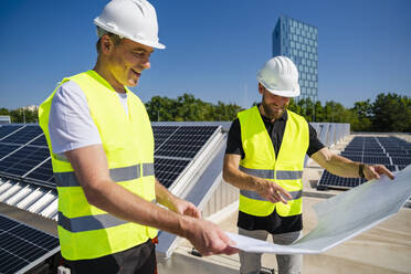 Zwei Techniker, die auf dem Dach eines mit Sonnenkollektoren ausgestatteten Firmengebäudes Strategien entwickeln - DIGF20296