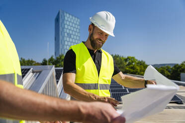 Zwei Techniker, die auf dem Dach eines mit Sonnenkollektoren ausgestatteten Firmengebäudes Strategien entwickeln - DIGF20297