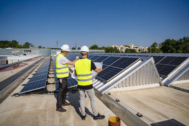 Zwei Techniker, die auf dem Dach eines mit Sonnenkollektoren ausgestatteten Firmengebäudes Strategien entwickeln - DIGF20300